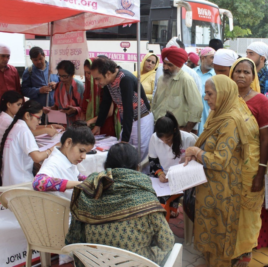 A group of people, primarily women, gather around a registration desk under a tent.